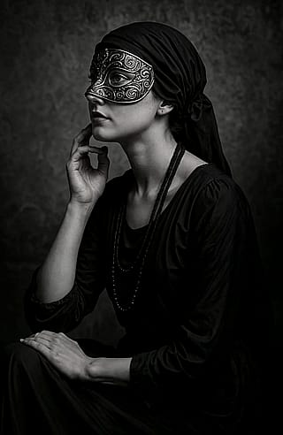 A moody, vintage-style black-and-white portrait showing a woman seated in profile, wearing a mask.'